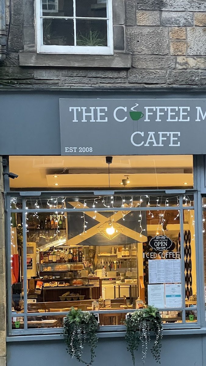 The Coffee Mill Cafe shopfront: a slate sign reading 'The Coffee Mill Cafe, est 2008' beside a window strung with fairy lights