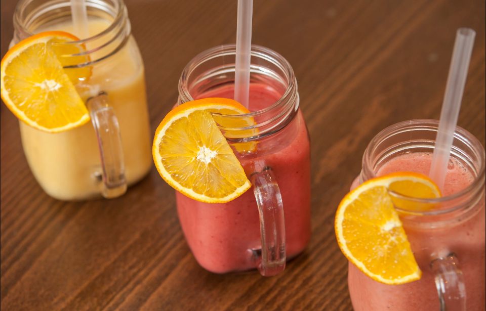 Three fruit smoothies in jars with orange slices